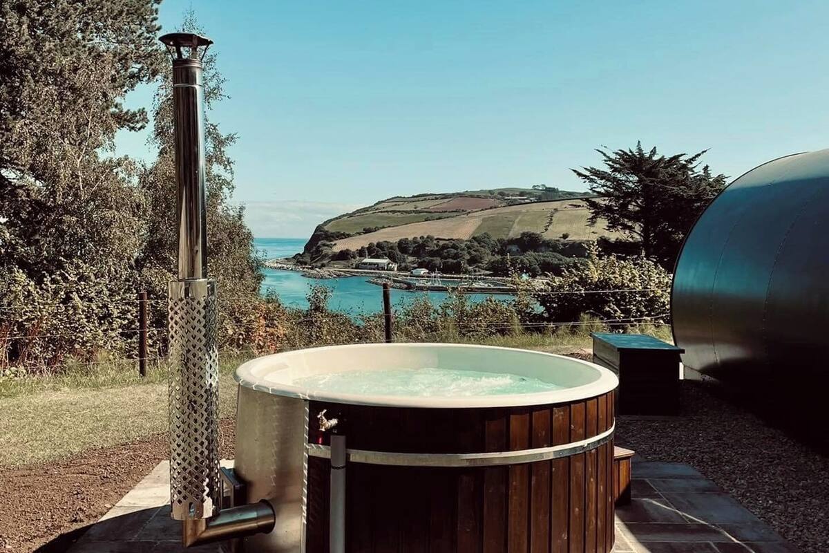 A hot tub with a wooden exterior, a metal chimney, and a view of a coastal landscape.