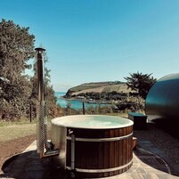 Un jacuzzi con revestimiento de madera, una chimenea de metal y vistas a un paisaje costero.