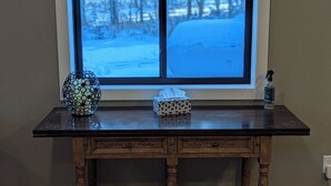 Una mesa de madera con un jarrón y una caja de pañuelos frente a una ventana con vistas nevadas.