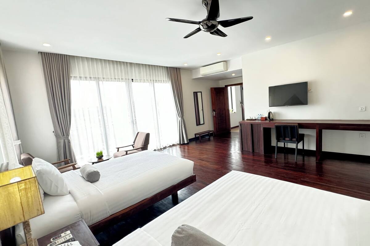 Una habitación de hotel con una cama grande, un escritorio, un televisor y un ventilador de techo.