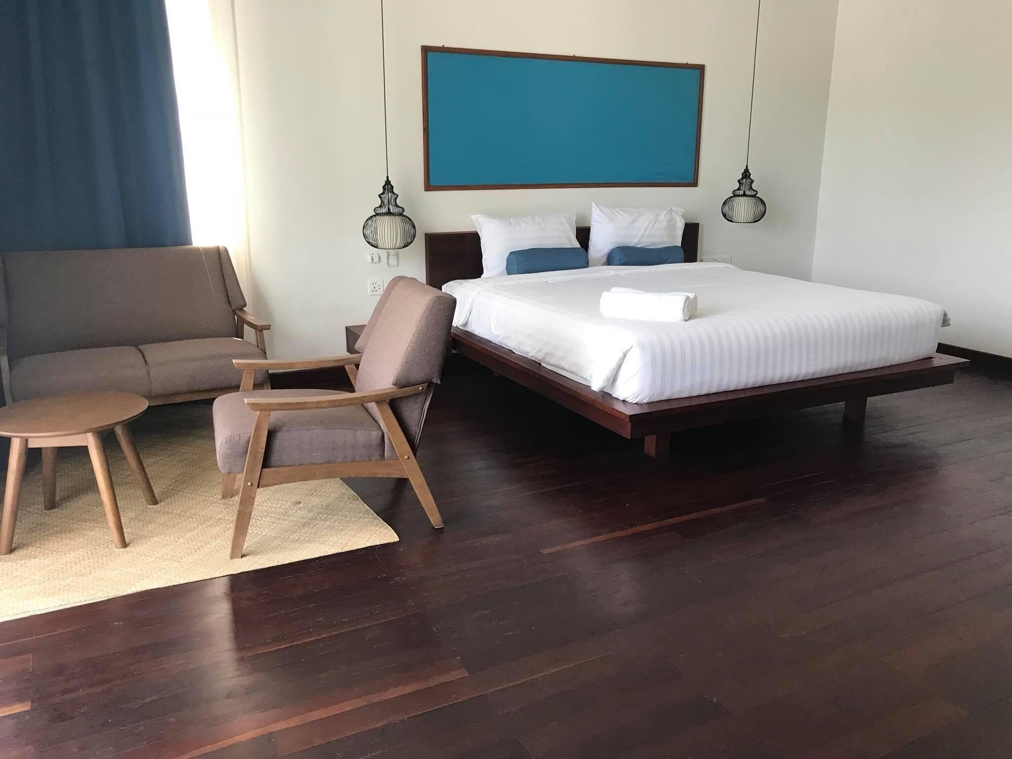 A bedroom with a large bed, a sofa, a chair, and two pendant lights.