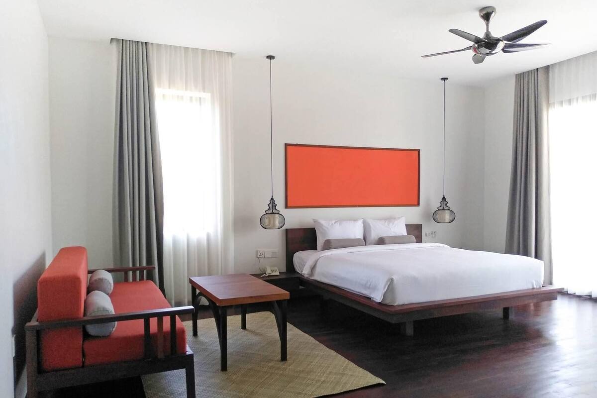 Habitación de hotel con cama, escritorio, silla y ventilador de techo.