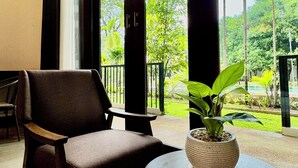 Ein Zimmer mit einem großen Fenster, einem Sessel, einem kleinen Tisch und einer Zimmerpflanze.