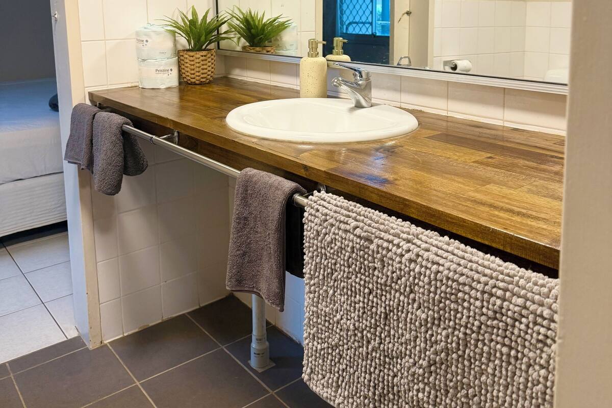 A bathroom with a wooden countertop, a white sink, a mirror, a towel rack, and a potted plant.