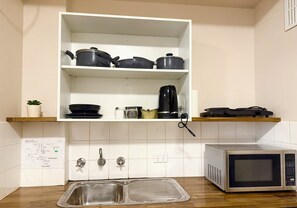 A kitchen with white cabinets, a stainless steel sink, a microwave, and a shelf with pots and a coffee maker. - Tropical River Hotel (Katherine)