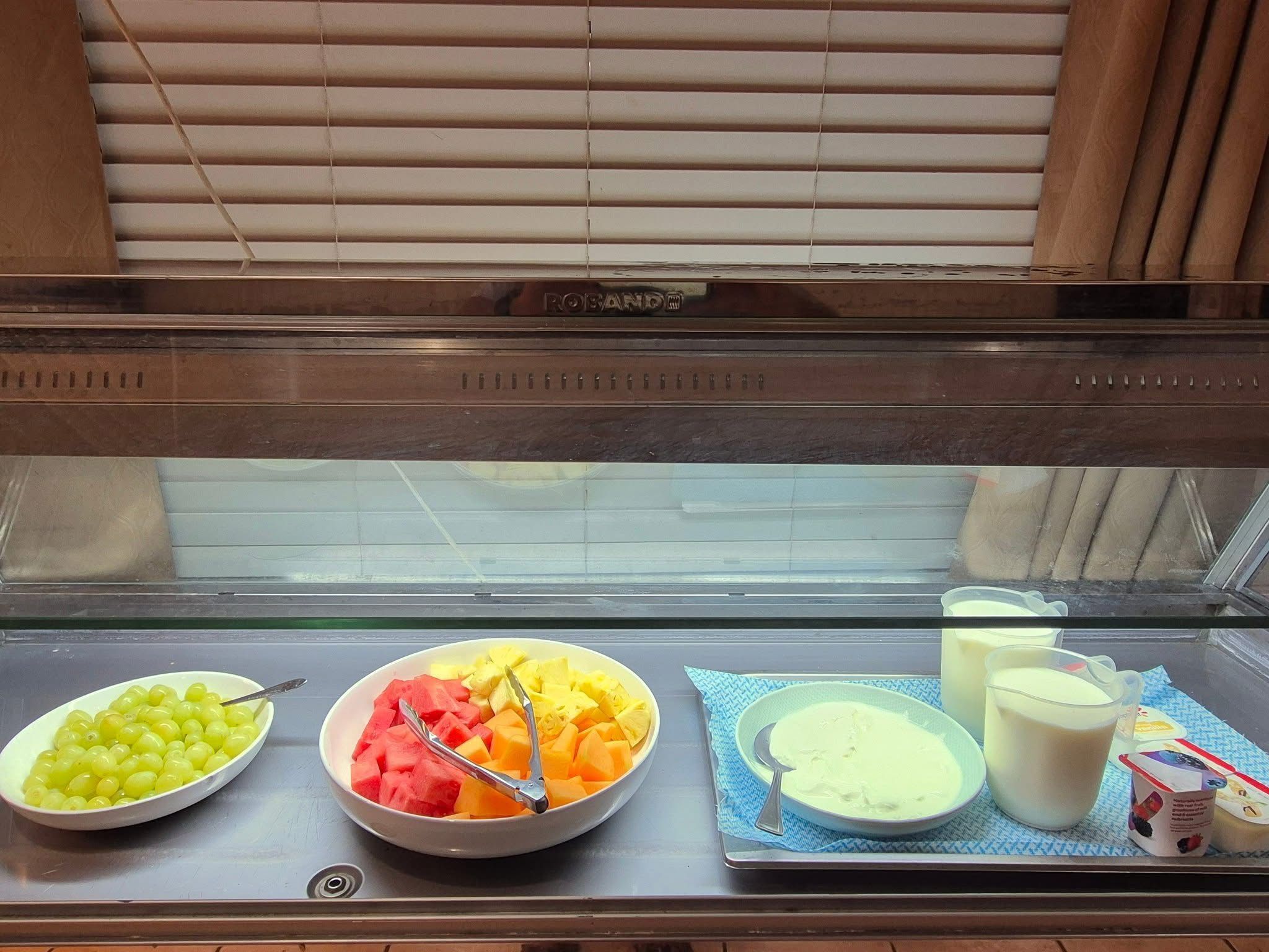 A buffet with bowls of fruit, a plate of soup, and a glass of milk.