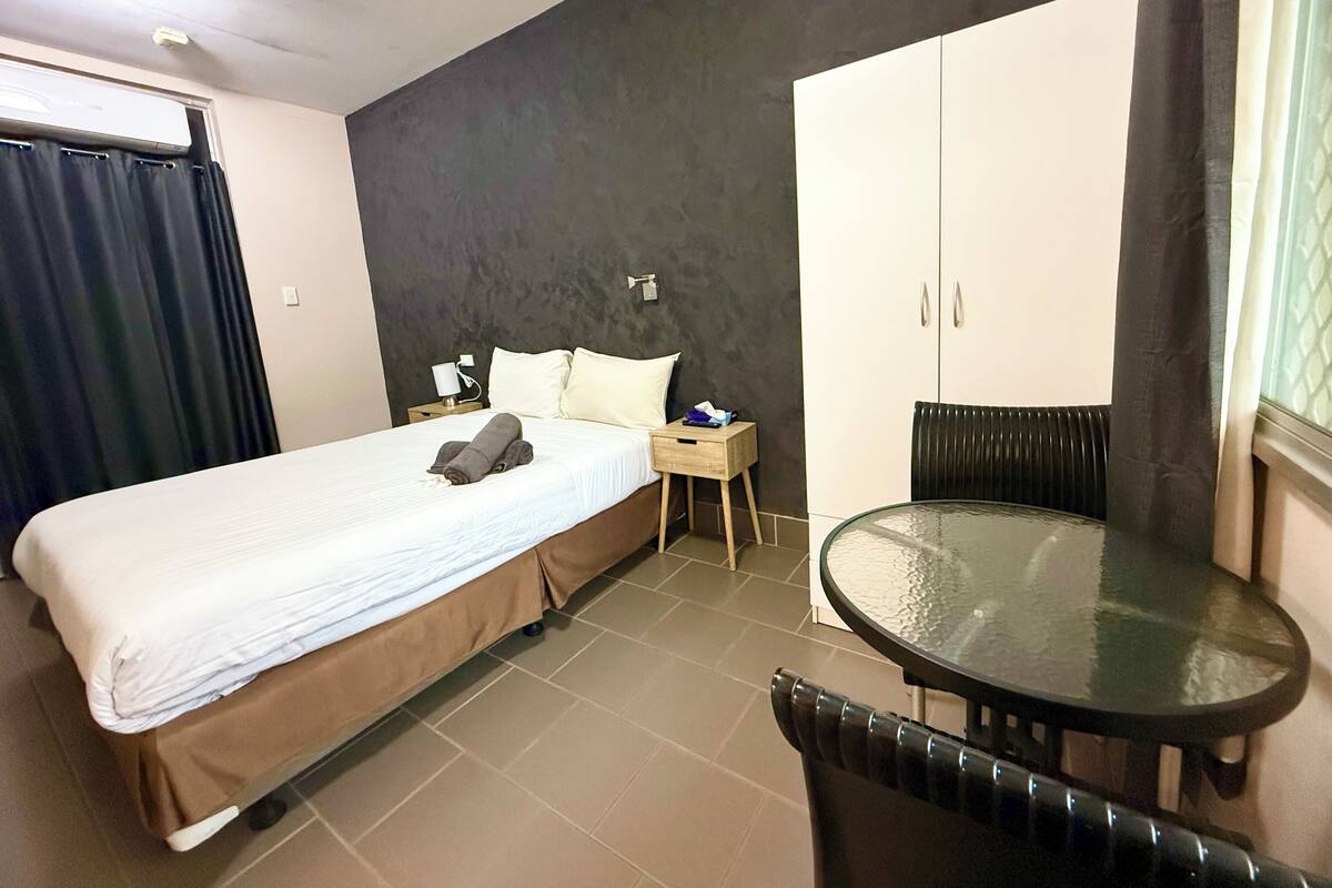 A hotel room with a bed, a nightstand, a table, and a wardrobe.