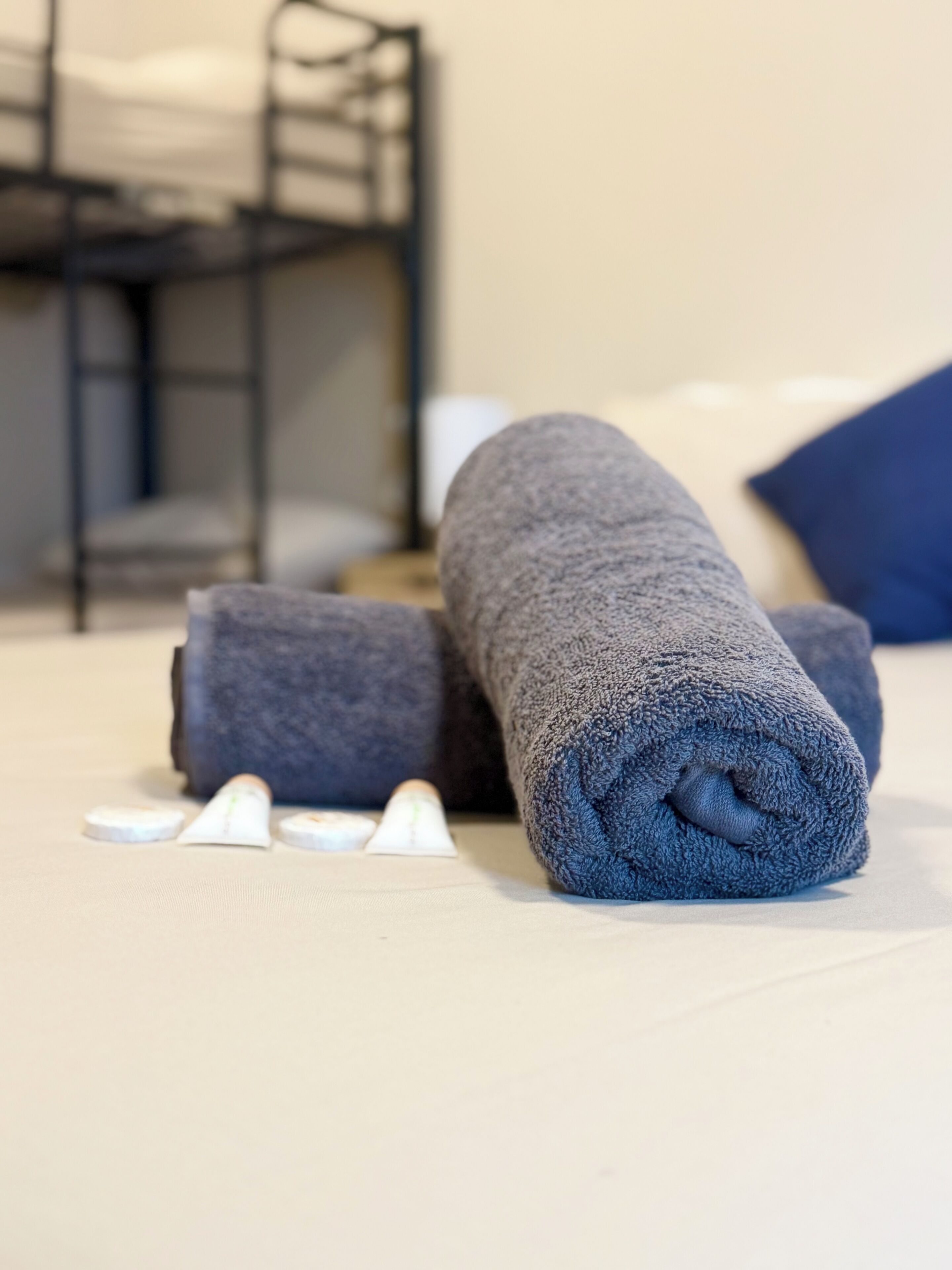 Un lit bien fait, avec des serviettes pliées, et un lit superposé en arrière-plan.