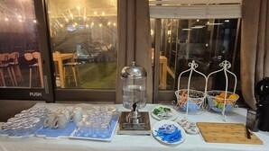 A table with various items including a water dispenser, plates of snacks, and a cutting board. - Tropical River Hotel (Katherine)