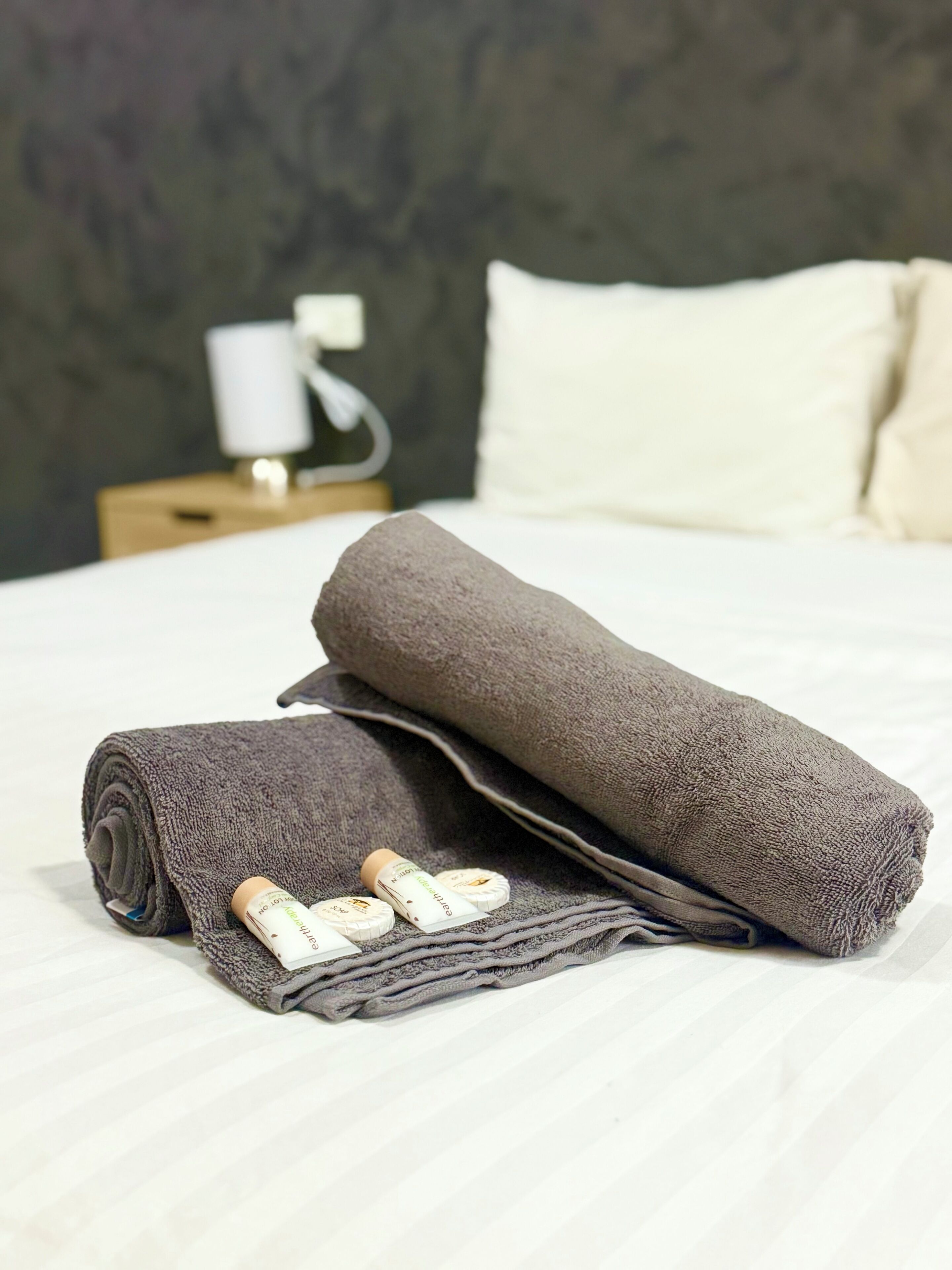 Una cama bien hecha con una toalla enrollada y dos botellas de loción al lado.