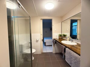 A modern bathroom with a glass shower enclosure, a wooden vanity with a large mirror, and a separate toilet area. - Tropical River Hotel (Katherine)