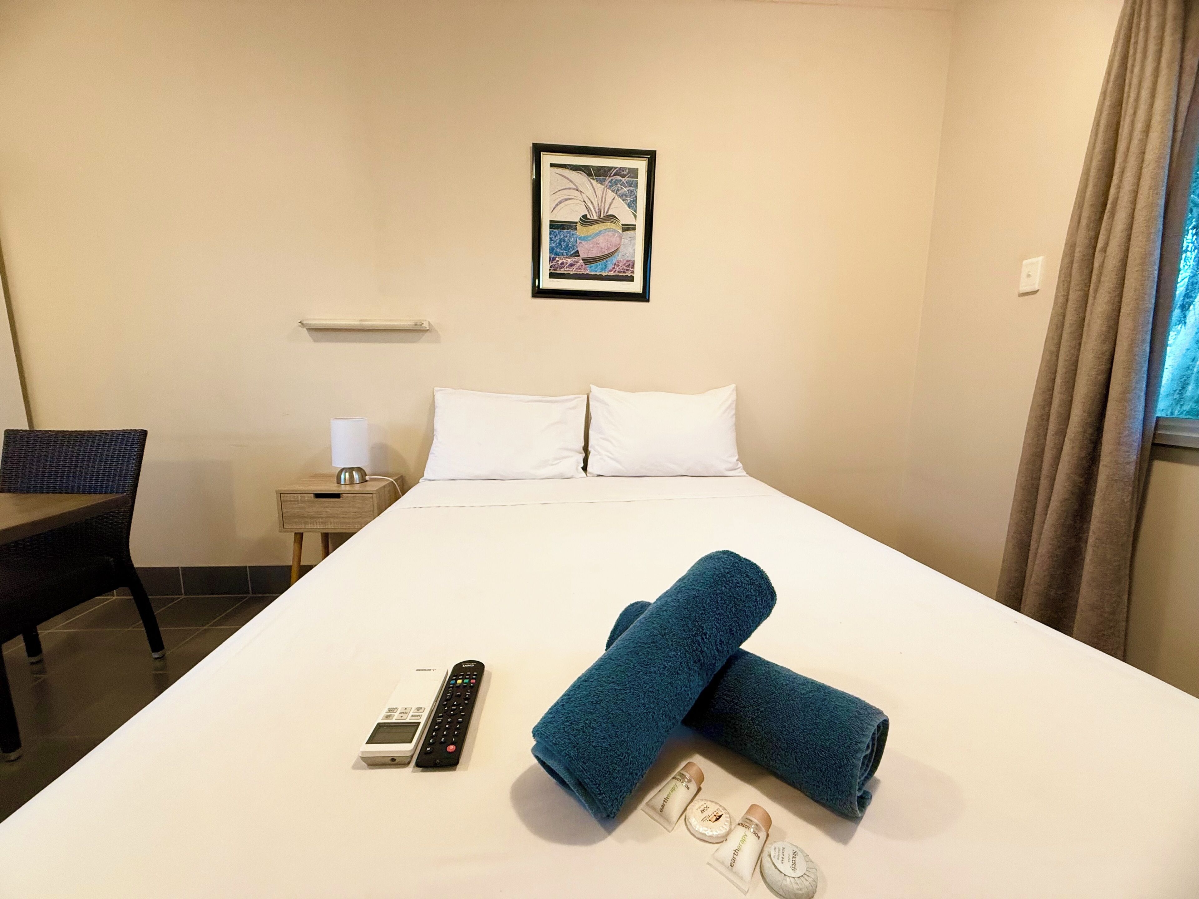A hotel room with a bed, a chair, a nightstand, a remote control, and toiletries.