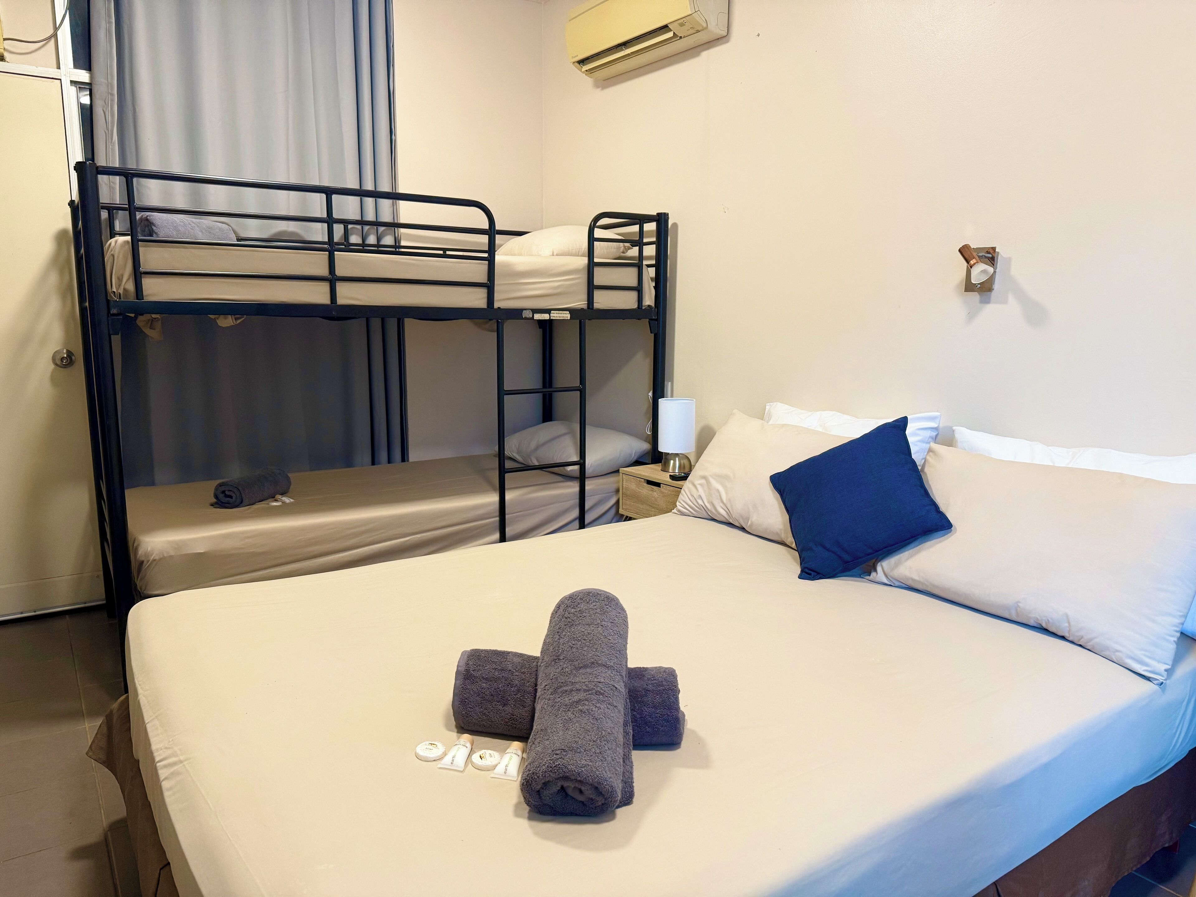 A bunk bed room with a single bed, a nightstand with a lamp, and a wall-mounted air conditioner.