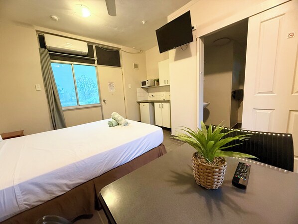 Ett hotellrum med en säng, ett litet pentry, en tv och en växt.