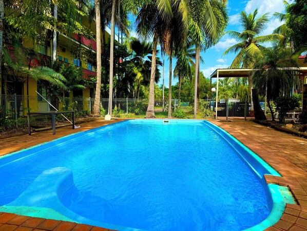 A swimming pool surrounded by palm trees and a fenced area. - Tropical River Hotel (Katherine)