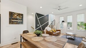 A modern living room with a wooden dining table, a sofa, and a painting of a piano. - Modern House minutes from Broadway (Nashville)