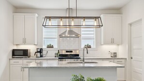 A modern kitchen with white cabinets, a central island, a stainless steel range hood, and a pendant light fixture. - Modern House minutes from Broadway (Nashville)