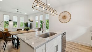 A modern kitchen with a large island, a built-in dishwasher, and a dining area with a table and chairs. - Modern House minutes from Broadway (Nashville)