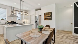 A modern kitchen with a central island, stainless steel appliances, and a dining area with a wooden table and chairs. - Modern House minutes from Broadway (Nashville)