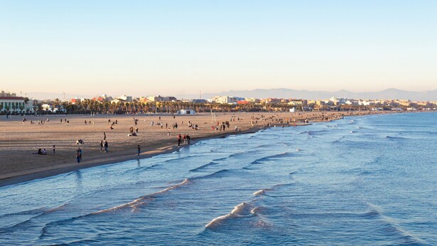 Un'ampia spiaggia con persone che camminano lungo la riva e onde che si infrangono sulla sabbia.