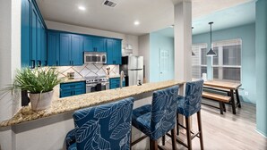 Una cucina moderna con mobili blu, un piano di lavoro in granito e un'area pranzo con tavolo in legno e sedie blu a motivi.