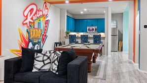 Un soggiorno con tavolo da biliardo, divano con cuscini decorati e un murale colorato.