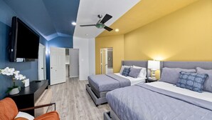 Una camera d'albergo con due letti, una televisione, una ventola a soffitto e una scrivania con una sedia.