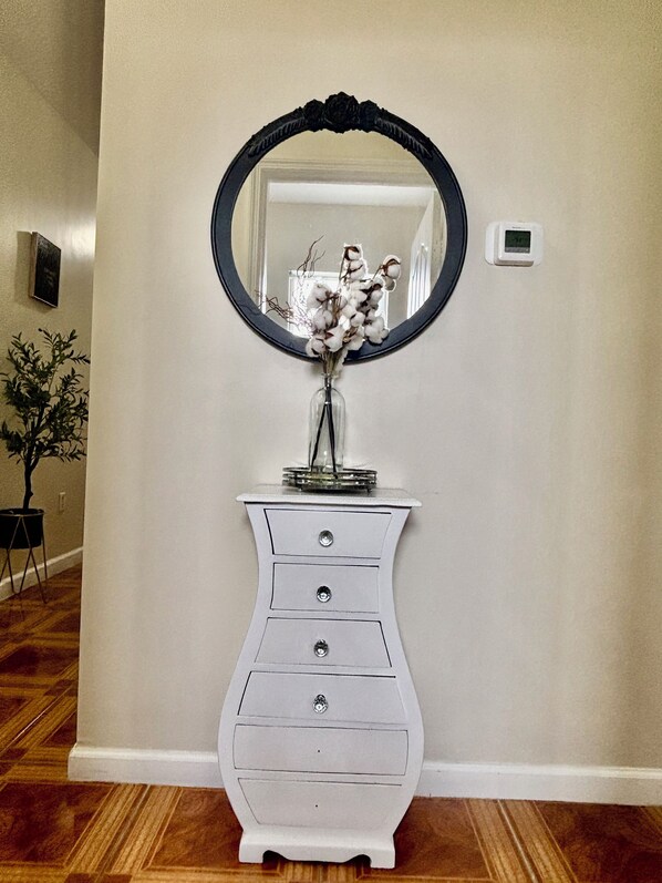 A white dresser with three drawers, a round mirror with a black frame, and a vase with cotton plants.