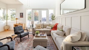 A modern living room with a sofa, armchairs, a coffee table, and a rug. There is a large window with a view of the city.