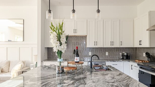 A modern kitchen with white cabinets, a marble countertop, and pendant lighting.
