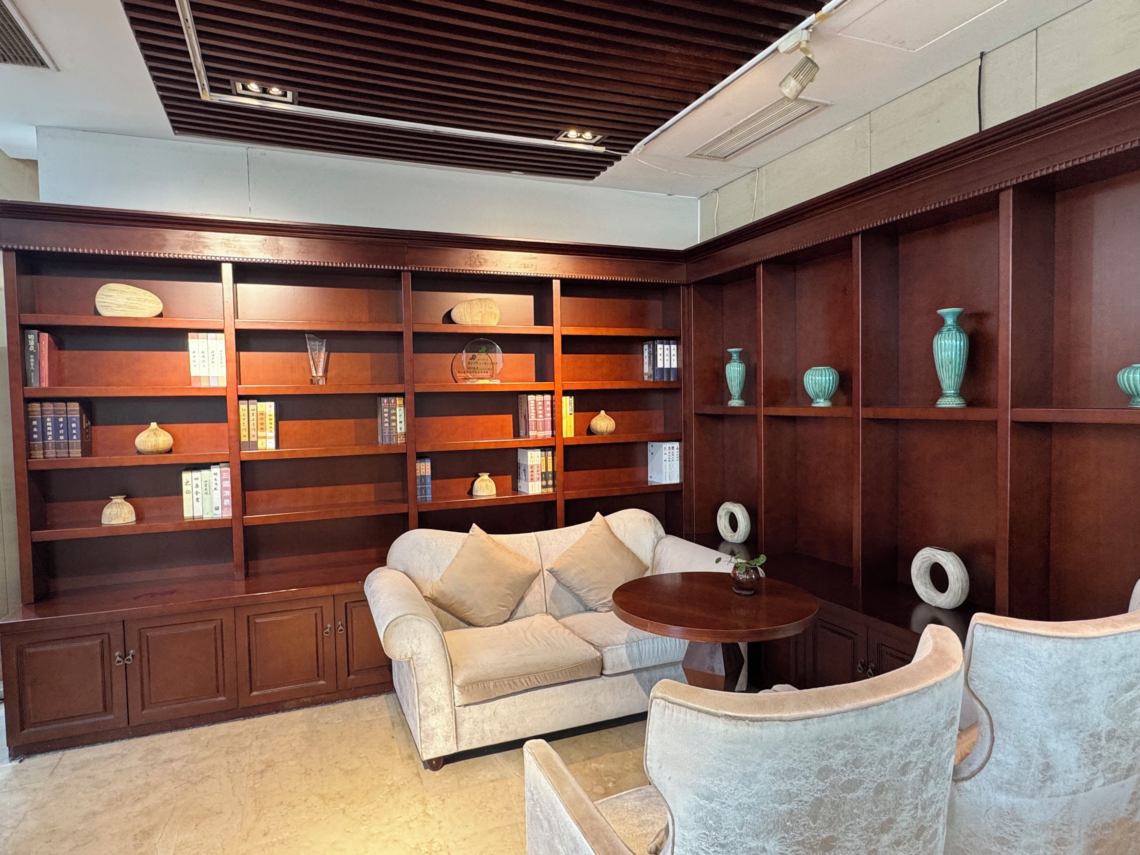 A room with a sofa, a round table, and wooden shelving with decorative items.
