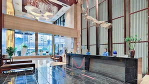 A modern hotel lobby with a reception desk, seating area, and large windows offering city views.