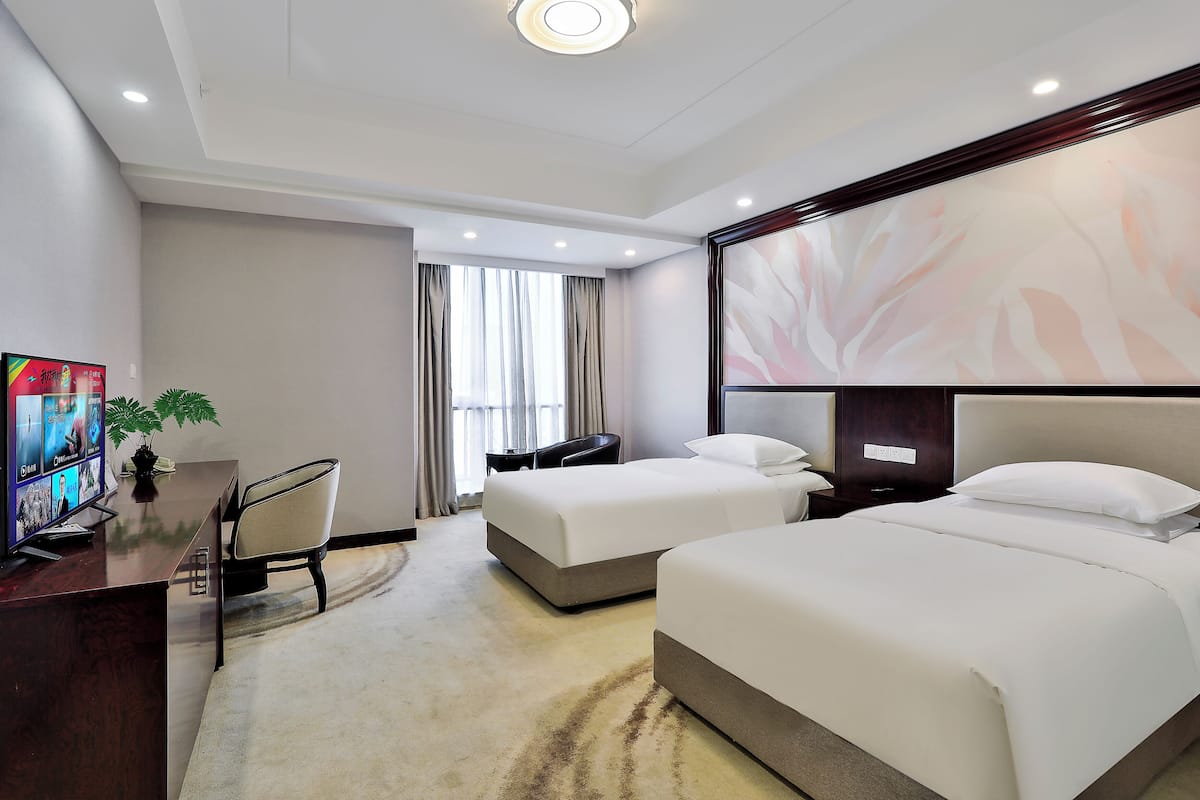 A hotel room with two beds, a desk, a chair, a TV, and a large abstract wall mural.