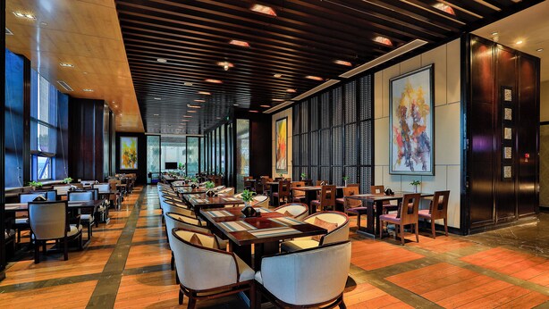 A spacious restaurant with long tables and chairs, high ceilings with wooden beams, and large windows allowing natural light.