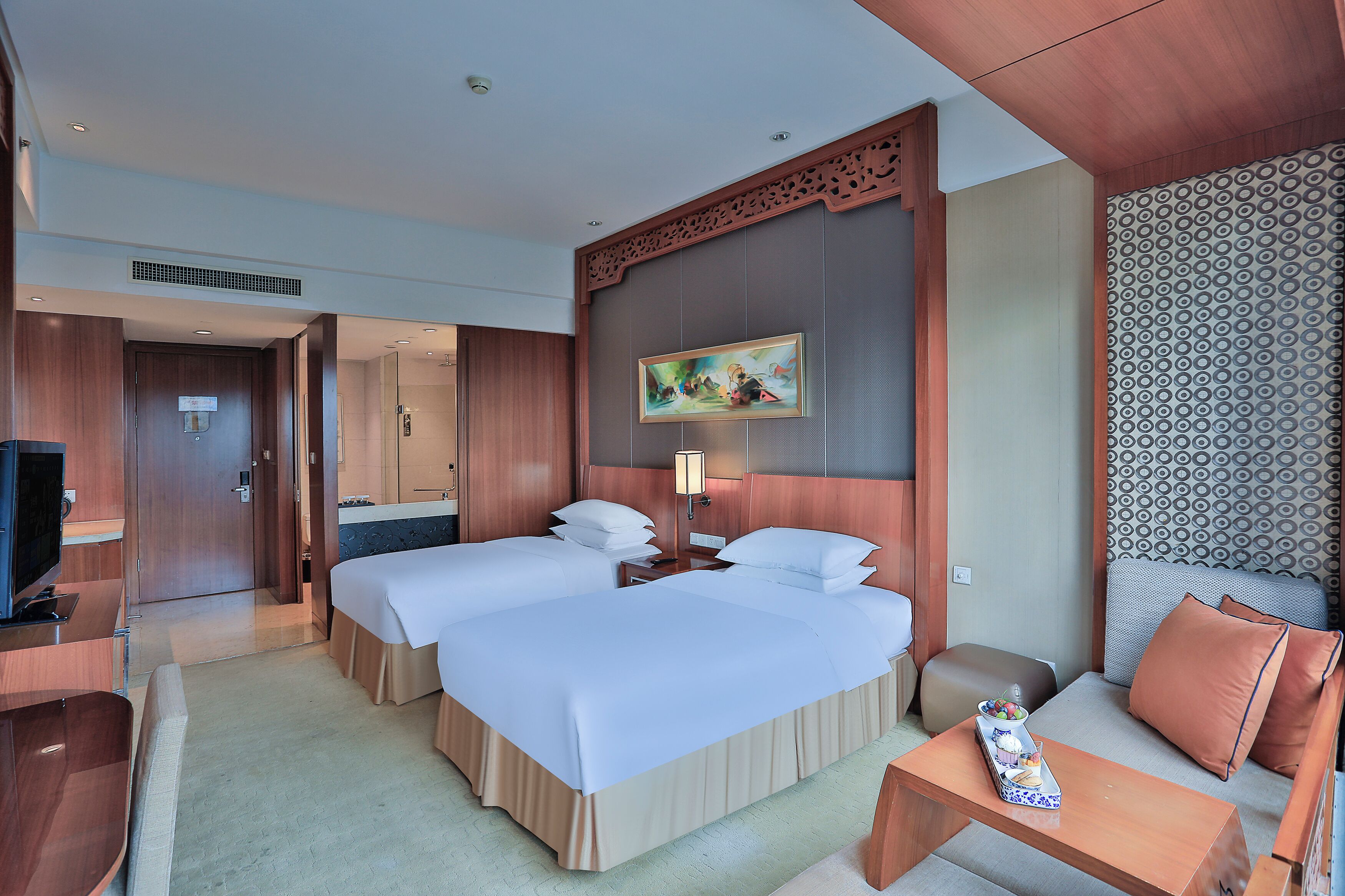 A hotel room with two beds, a TV, a desk, and a sofa.