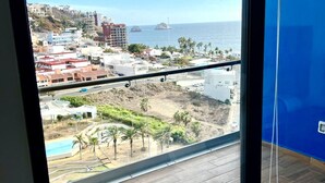 A balcony with a view of a coastal cityscape, including buildings, a beach, and palm trees. - Boca de cielo Apartments (Mazatlán)