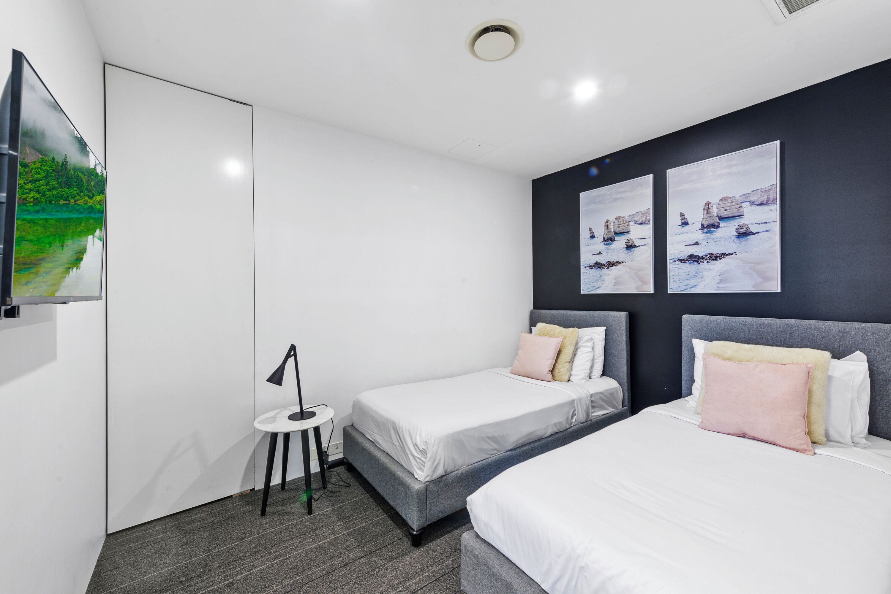 A modern hotel room with two beds, a small table, and artwork on the wall.