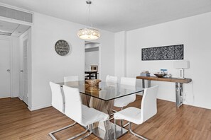 Un espace repas moderne avec une table en verre, des chaises blanches, un luminaire suspendu et un élément décoratif mural.