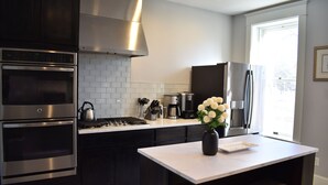 A modern kitchen with stainless steel appliances, a white countertop, and a vase with flowers. - Historic Manor Overlooking Park (Bloomington)