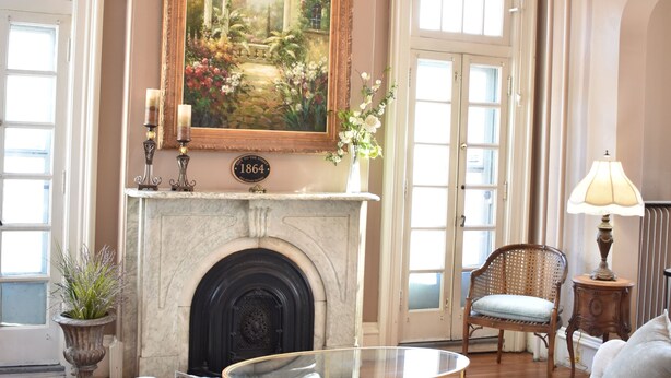 A room with a fireplace, a sofa, a chair, a table, and a chandelier. - Historic Manor Overlooking Park (Bloomington)