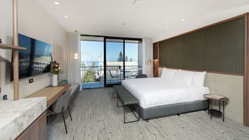 A hotel room with a large bed, a desk with a chair, a TV mounted on the wall, and a balcony with a view of a Ferris wheel.