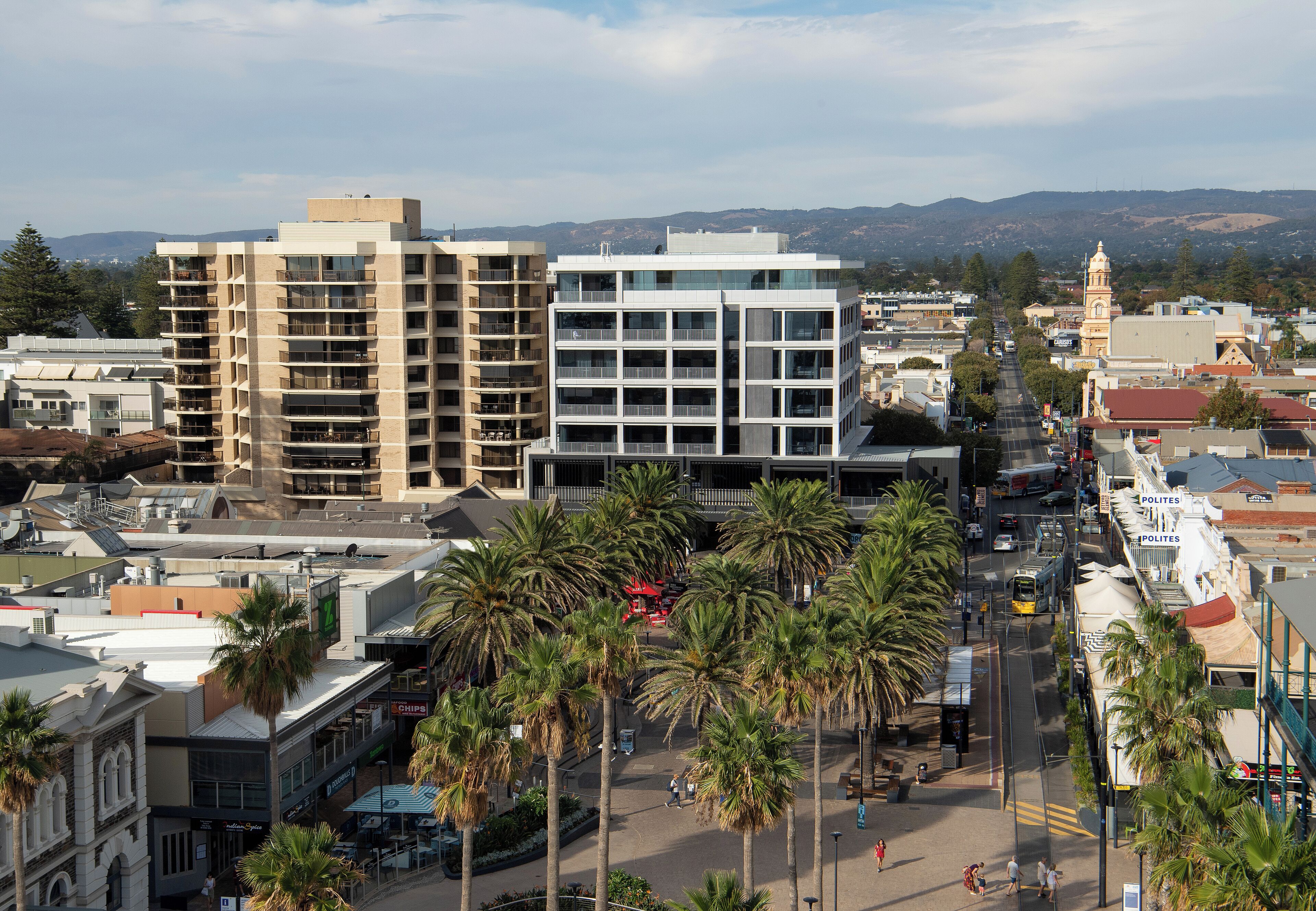 A multi-story building with a modern design, surrounded by palm trees and a street with vehicles.