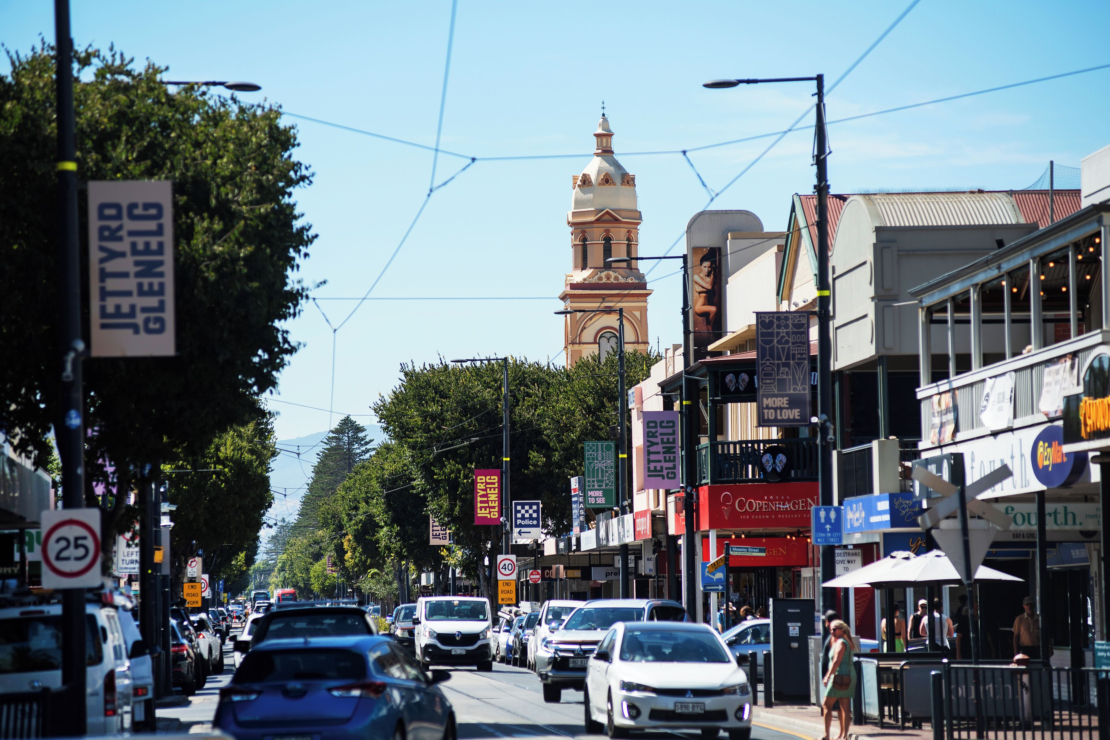 A busy street with shops, a clock tower, and tram lines.