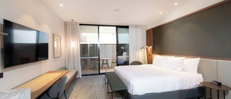 Una habitación de hotel moderna con una cama grande, un escritorio, un televisor de pantalla plana y una puerta de vidrio corrediza que da a un balcón.