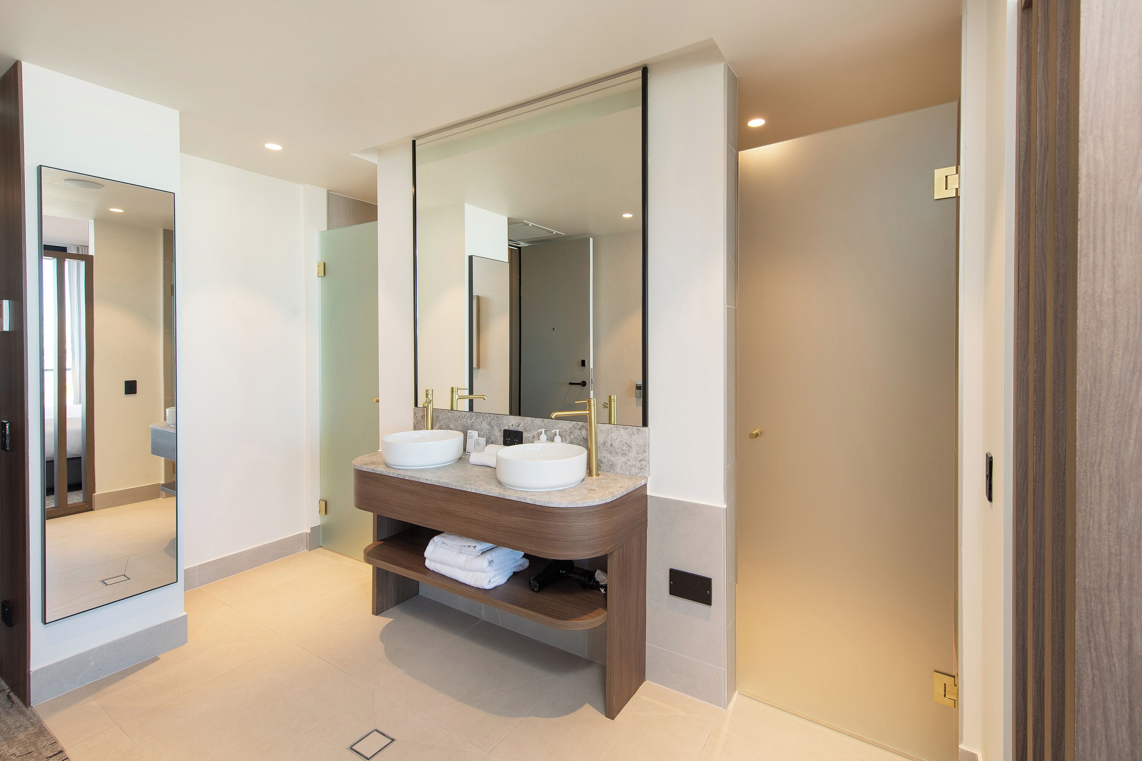 A modern bathroom with two sinks, a large mirror, and a wooden vanity.