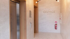 A modern hallway with a wooden panel wall, a ceiling light fixture, and a fire extinguisher. - The George (Glenelg)