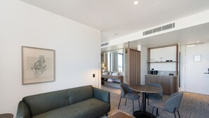 A modern living area with a sofa, chairs, a coffee table, and a kitchen in the background. - The George (Glenelg)