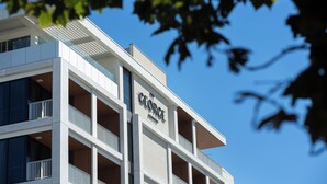 A modern building with a prominent "George" sign, multiple balconies, and a clear blue sky in the background. - The George (Glenelg)