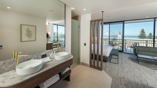 A modern bathroom with a large mirror, two sinks, and a view of the sea through large windows. - The George (Glenelg)