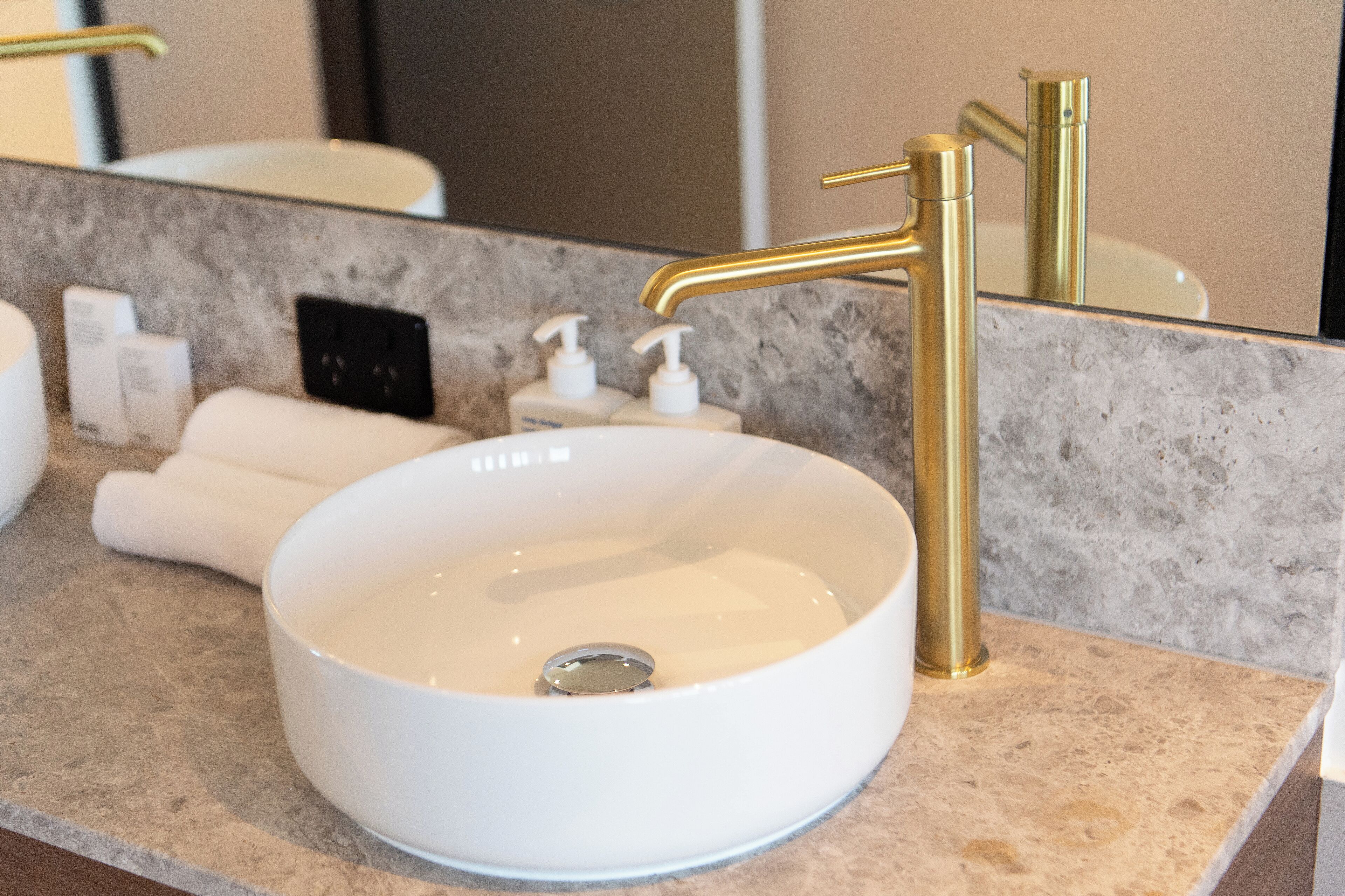 Une salle de bain avec un lavabo blanc, un robinet doré et un comptoir en marbre.